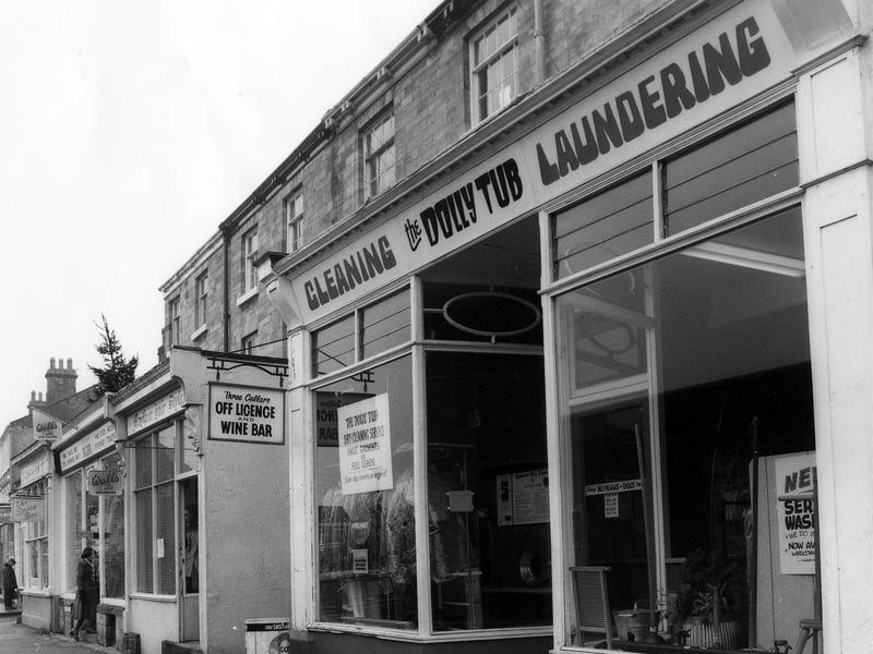 A row of shops on Boston Spa High Street in March 1979. In the foreground is the Dolly Tub Launderette, with the entrance to the Three Cellars off licence and wine bar to the left. Next to this is Mayfair Hair Studio, then a shop selling fancy goods, stationery and ice cream. On the end of the row is the Spice Box restaurant.