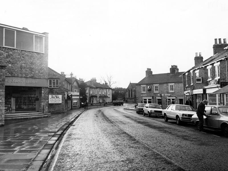 Looking north-west along Westgate with Wetherby public library on the left, followed by the Gold & Watch shop, jewellers, Renfree & Helliwell, estate agents, and the Blue Bird Cafe. Across the road is the New Inn public house, and shops including Double A travel agents, Bradford & Bingley building society and Joan Sutcliffe Gifts. Cars are parked on the right. Pictured in May 1979.