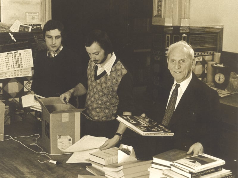 Three members of the Porters team at Leeds Central Library in April 1977. Clive Wroe is in the centre. The team are unpacking boxes of books on the third floor of Leeds Central Library near the north staircase.