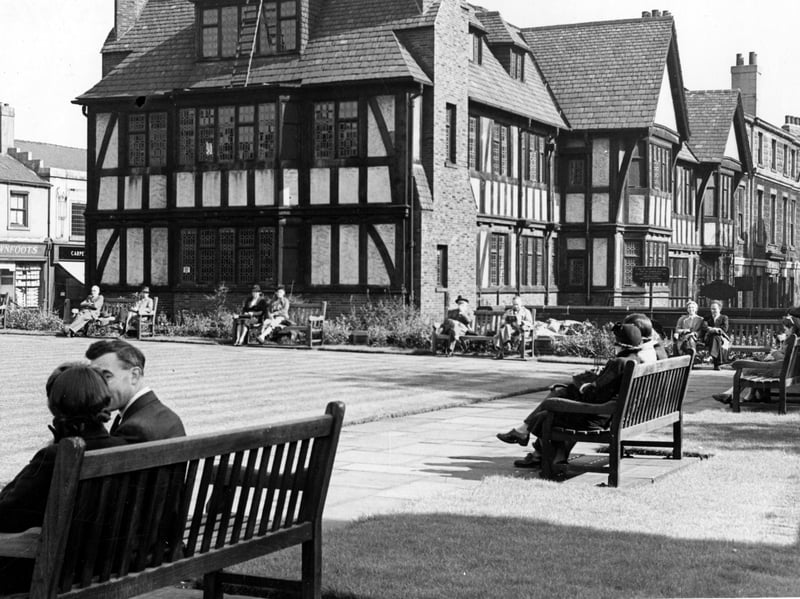 The rest garden on Merrion Street in September 1943.In the foreground people are sitting on park benches arranged around a central square lawn. Behind are Tudor style houses. On the left, E. R. Brownfoot (blind maker)can be seen on number 38 Merrion Street.