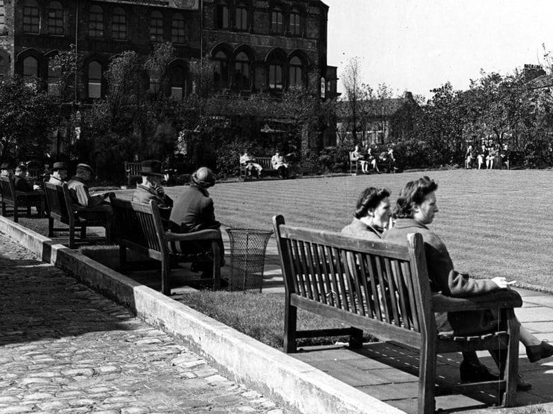 Looking south at the rest garden on Merrion Street. People sit on park benches arranged around a central square lawn. Behind is L. & M. Dombyack, furriers, at number 35 Wade Lane. Pictured in September 1943.