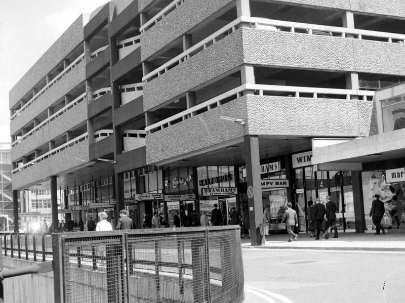 Side view of the Merrion Centre from the service road. Shops visible include Halfords, Coombes leather goods, Bramhams bacon specialists, Wimpy Bar and the Midland Bank. The Merrion Centre car park is visible above the shops.