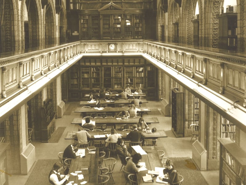 Looking from the gallery down to the Reference Library on the second floor of Leeds Central Library. This room is on the south side of the building and fronts onto The Headrow. Many people are seated at the long desks studying or reading.