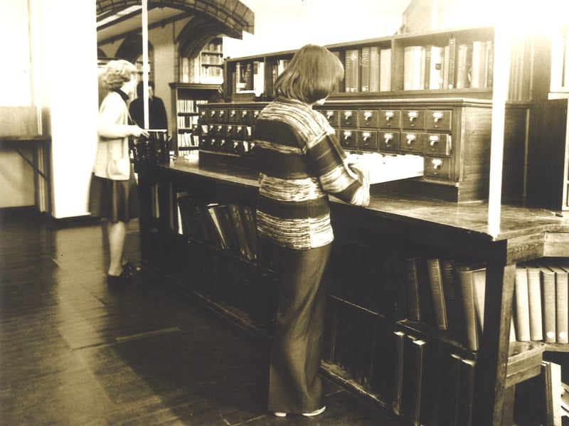 This photo shows part of the Reference Library on the second floor of Leeds Central Library, facing onto The Headrow. A member of staff is looking through card catalogue drawers. This is now the Local and Family History Library.