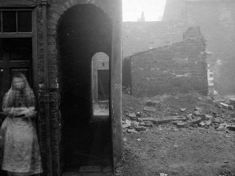 Cross Myrtle Street in January 1902. It was located in the Pottery Fields area, site of former Leeds Pottery. View of house with shawled woman in doorway. A covered passage way (also called a snicket or ginnel) led through to back of property.