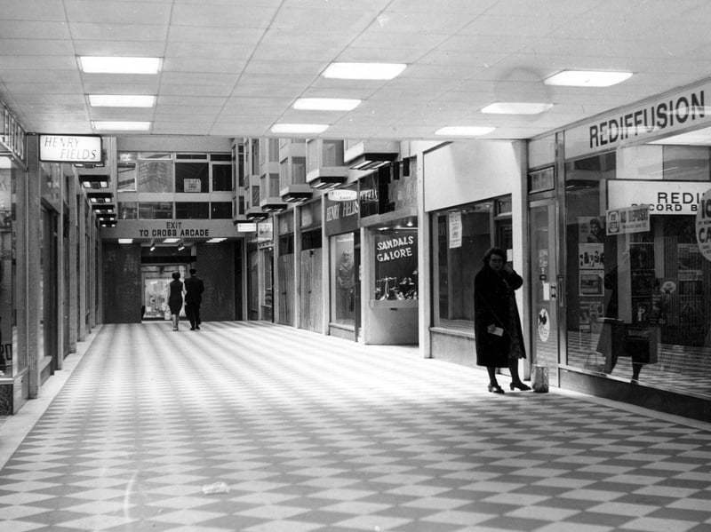 Inside the Empire Arcade looking down towards Cross Arcade. Shops visible include Henry Fields and Rediffusion. A man and a woman walk down to the Cross Arcade exit.