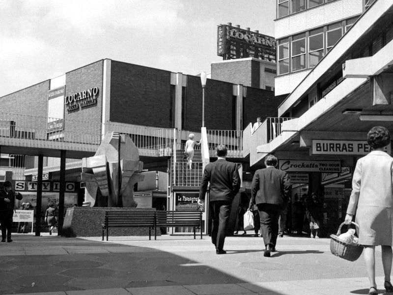 The sculpture 'Androgyne' by Glenn Hellman outside the Merrion Centre. A sign for the Locarno Mecca Dancing can be seen on a building in the background. Shops visible include Stylo shoes and Crockatts 2 hour cleaning.