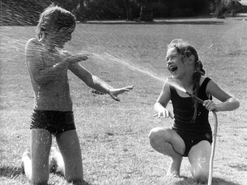 Joanne Bailiff, 10, and Charles Patrick, 11, from the summer play scheme at Broad Lane Middle School, Bramley, play with a hose in August 1981
