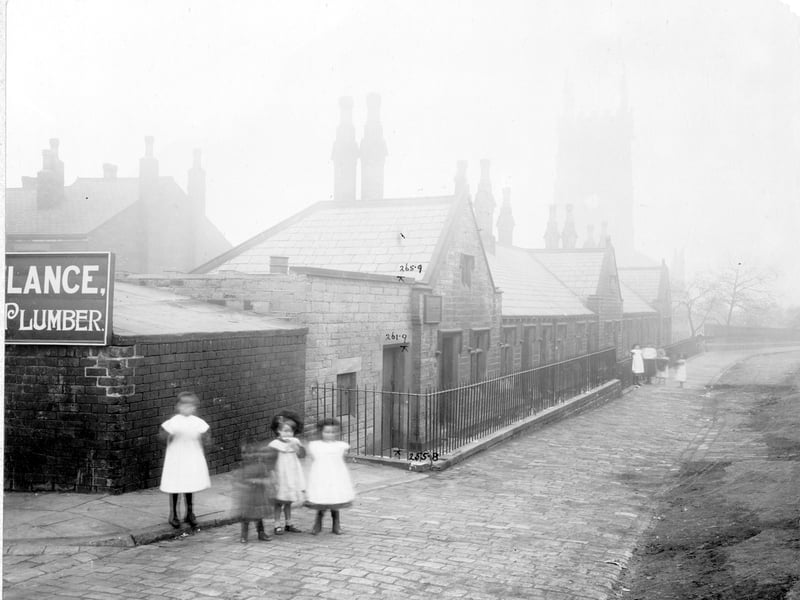 Row of nine dwellings, built around 1838, gift of benefactor Josias Jenkinson who had left other property and charitable funds to the people of Leeds, founded in 1643. On the left premises of Frank Roylance plumber. To the right is St Mark's Church and churchyard. Pictured in October 1905.