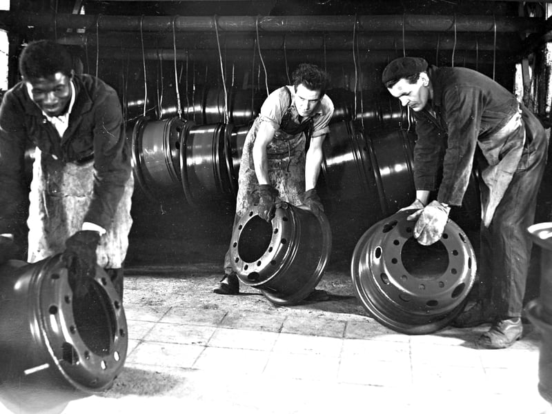 Working alongside a overhead dipping line, three men lift heavy steel vehicle wheels at the GKN Sankey works in Hadley, likely captured between the mid and late 1960s. As one of Shropshire's largest engineering employers, the busy Castle Works produced millions of wheels, pressings, and components for Britain's automotive industry. This striking image highlights the skill, heavy labour, and strong industrial camaraderie that defined everyday working life in the factory. Did you or a family member work on the shop floor at GKN Sankey in Hadley during the 1960s, or do you recognise anyone in this photograph?
