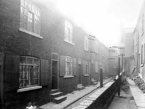 This photo from May 1904 shows the Blackman Lane improvements planned for the back of the Pleasant Dairy. Image shows a narrow alleyway split in half. On one side are long terraced buildings with shutters around the windows and pavement outside. On the right is another long terraced row this time with the opportunity to grow plants and flowers. Future improvements are marked on the image.