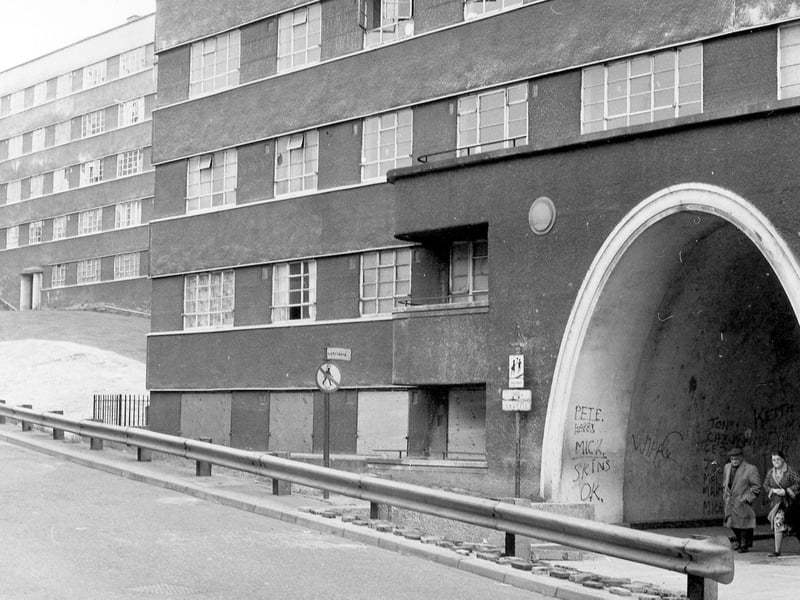 Two people are seen coming through one of the arched entrances at Quarry Hill Flats circa 1974/75. The photo shows the flats in a dilapidated state with some broken window panes.