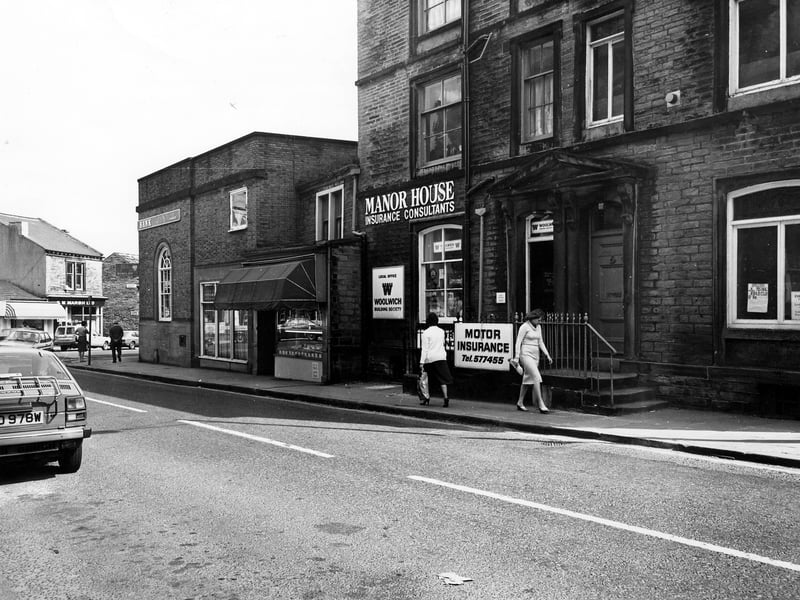 Manor House Street showing from left Barclays Bank, then W.H. Bowman, butchers, Manor House insurance consultants including the local office of the Woolwich Building Society, and on the right the offices of St. John's Ambulance Brigade. In the background on the left the junction with Lowtown can be seen, with shops including G.W. Marsh, TV rental. Pictured in April 1982.