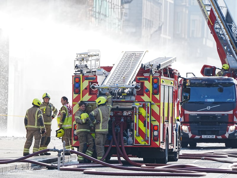 Firefighters and a fire engine at the scene of a blaze, with smoke in the background