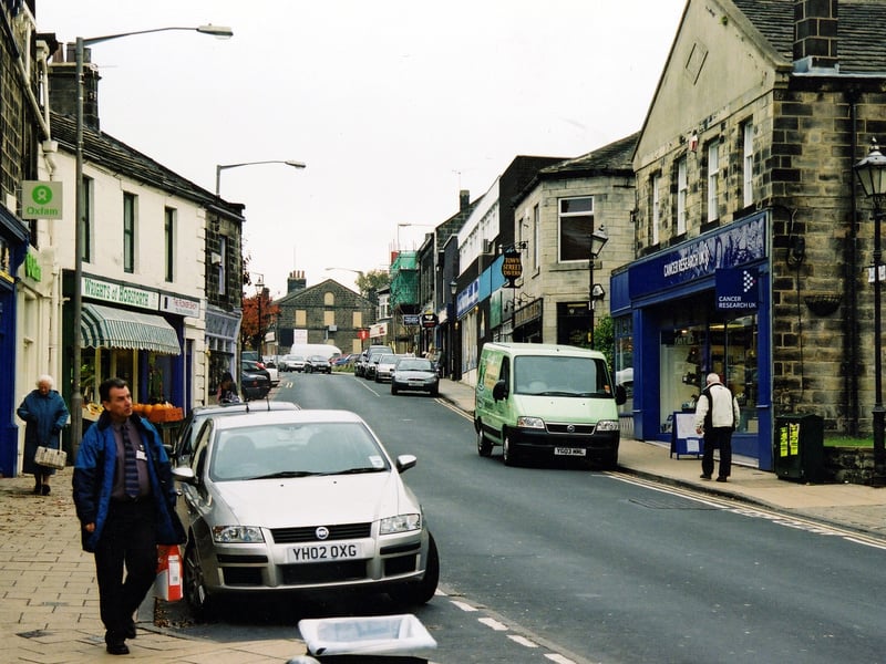 Town Street showing shop premises. Several of these are charity shops, Oxfam and Sue Ryder on the left and Cancer Research U.K. on the right. The Town Street Tavern is also visible on the right. Pictured in October 2003.