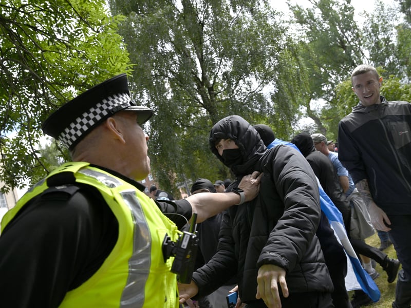 A police officer holds back a demonstrator with his face covered during an anti-immigration protest organised by Unite the Clans Scotland, after objects were thrown towards a Stand Up to Racism counter-protest, at Glasgow Green.