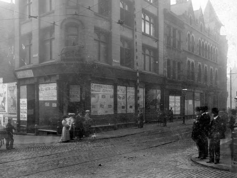 The junction of New Market Street with Kirkgate former premises of Tiger Stores. Statue of tiger sited above doorway. Women, men and children in period dress pose on corners of roadside. Pictured in July 1907.