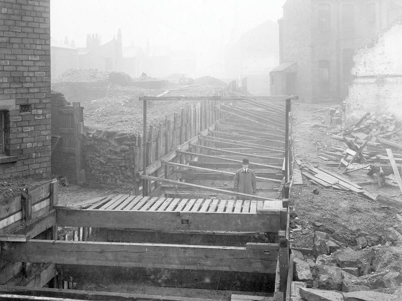 Demolition of derelict site in Moscow Street and Hope Street showing a trench supported by wooden planks. A man in a bowler hat and overcoat is standing the trench. Pictured in December 1907.