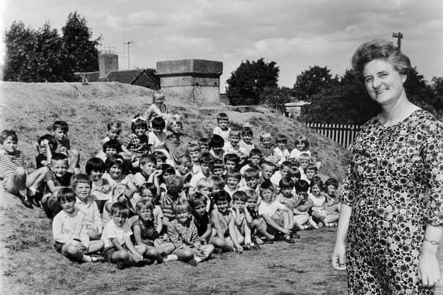 Miss H M Oliver stands proudly beside her pupils in this archive photograph date-stamped 25 July 1969. The former headmistress of Shrewsbury Coton Mount Infants had moved on to lead Meole Brace C of E Infants School when this end-of-term portrait was taken. Gathering the children outdoors, the class sits gathered against an earth-mounded air raid shelter, a leftover piece of wartime history that served as a familiar playground feature for generations of Shrewsbury schoolchildren. Were you one of the pupils pictured with Miss Oliver in 1969, or do you remember playing around the old air raid shelter at the school?