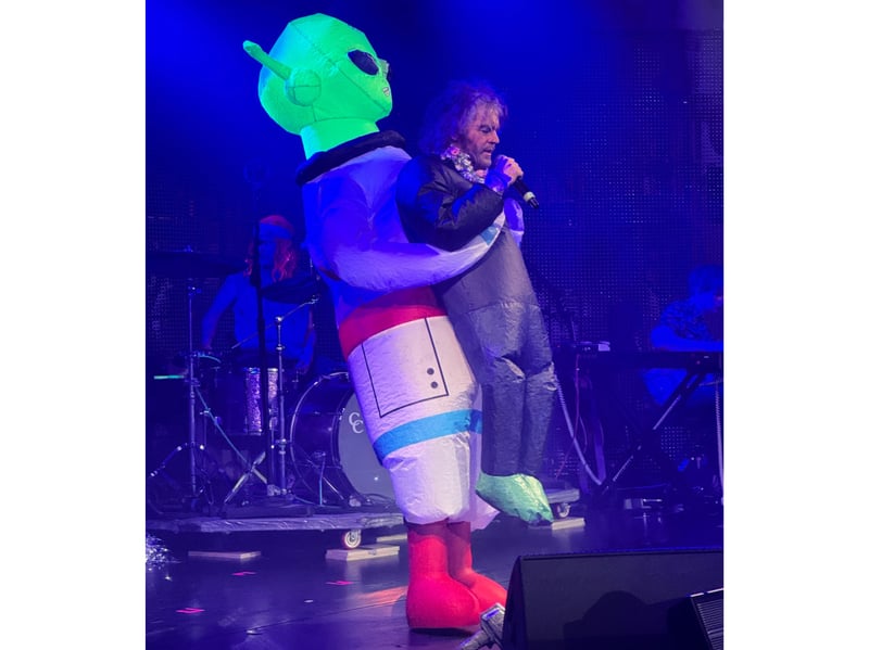 Wayne Coyne has a little break, carried by a large alien.
