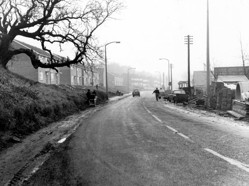 Pudsey Road, just east of the Ring Road. People, traffic and houses visible. Construction work to the right. Street lights and telephone poles visible. Pictured in December 1968.