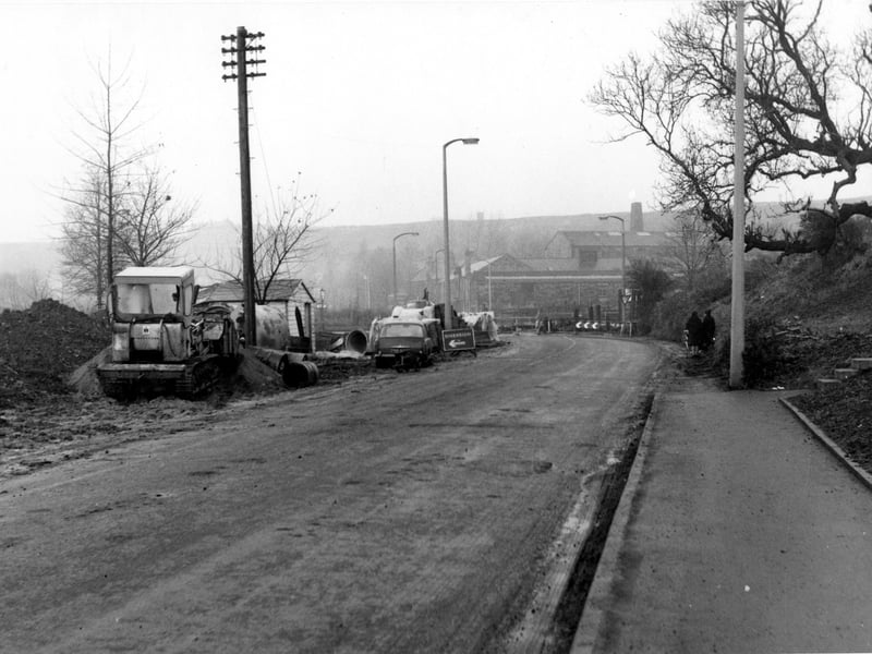A view looking along Pudsey Road in December 1968. Roadworks and diversion signs visible, also parked cars and a bulldozer. Two women are walking along the street. A bus can be seen in the distance. Junction with Henconner Lane visible.
