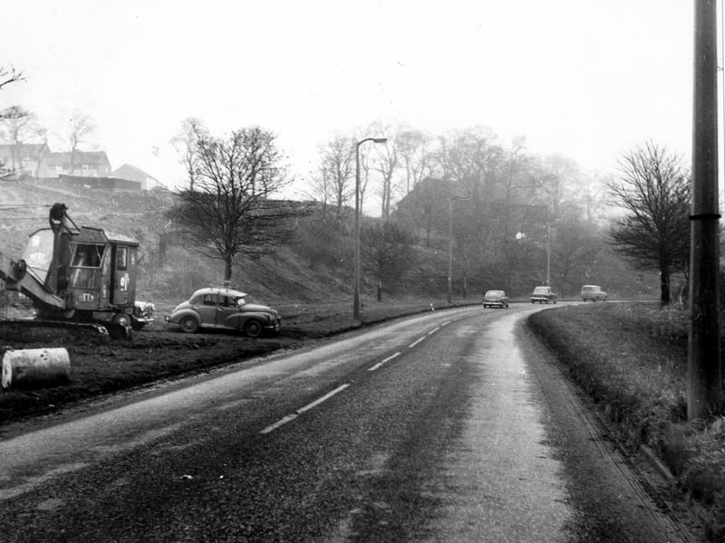 Looking east north east down Bramley Ring Road. The Spring Valley Estate can be seen on the left. Cars are on the road and one is parked to the left near a construction crane with tank tracks.