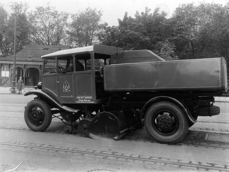 A tram track sweeper in operation outside the main entrance to Roundhay Park on Princes Avenue. A young boy with a bicycle looks on, background left, in front of the tram shelter and ticket office. Pictured in October 1934.