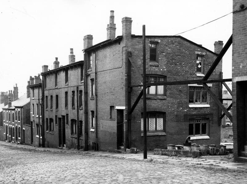 A row of back-to-back terraced houses on Abbott Terrace in  August `1967. Number 21 is located in the gable end of the terrace where the terrace is split and wooden supports brace the building. Here dustbins are lined up and Abbott Road is just visible.