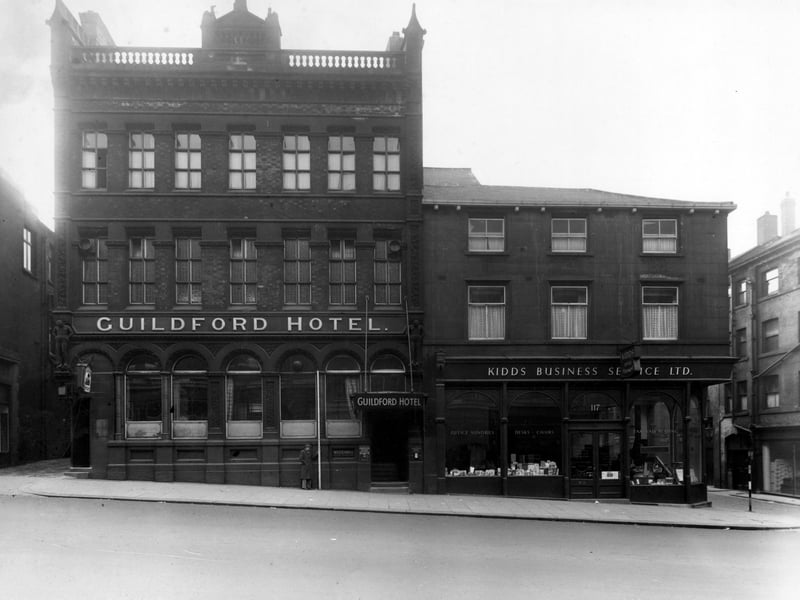 The south-west side of The Headrow showing number 115 The Guildford Hotel and number 117 Kidds Business Service Ltd. To the far left is the entrance to Green Dragon Yard, to the far right is Basinghall Street. A Tetley pub sign is visible. Pictured in December 1949.