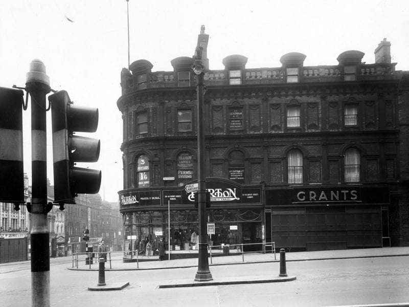 The south side of The Headrow, at its junction with Briggate. Shops shown are 'Grants Furriers', and 'Montague Burton Ltd, Tailors'. To the left on Briggate, 'W.Greenwood and Sons, jewellers' is visible. A set of traffic lights are prominent on the left. Pictured in December 1949.