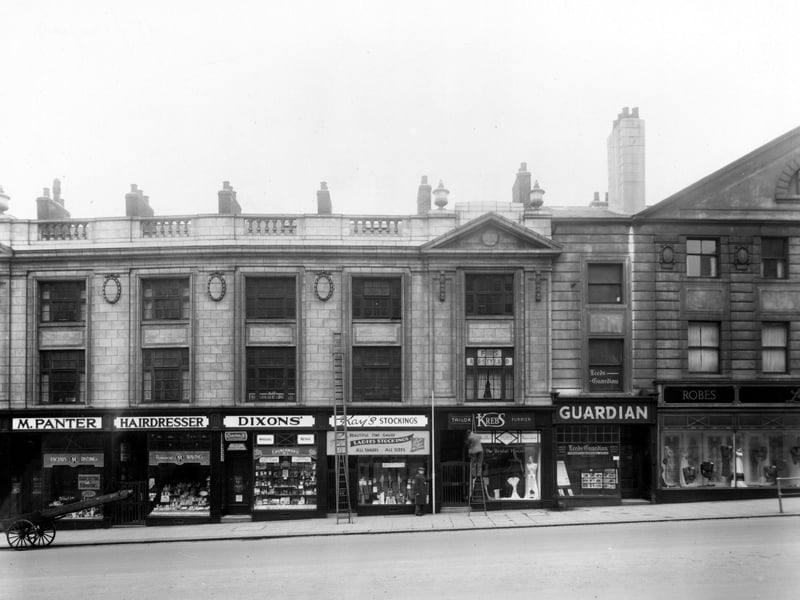 The South side of The Headrow, showing the following Premises, numbers 31/33, M. Panter, hairdresser, number 35, J.R. Dixon and Sons, tobacconist. Number 37 is Kays Hosiery, number 39, H. Krebs, furrier, number 41, West Leeds News Ltd, publishers, and number 43, Lucette (Leeds) Ltd, gowns. On the left is a handcart. Ladders are propped against the shops, and a man has climbed one of them. A man stands holding a measuring stick.