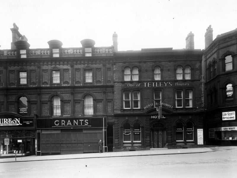 The south side of The Headrow showing number 47 Montague Burton Ltd. tailors, 49 Grants furriers, 51 Horse and trumpet hotel, 55 Lea-Scott Ltd. opticians. A man stands holding a measuring sticks. A poster for the Empire Theatre is visible. Pictured in December 1949.