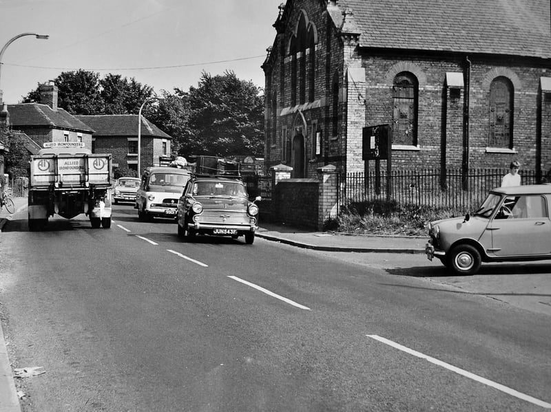 Classic motor vehicles make their way along the road past the local church in this lively street scene from Hadley. Featuring an Allied Ironfounders lorry, a luggage-laden saloon car registered in 1967 (JUN 543F), and a classic Mini parked on the roadside, the snapshot captures the daily hustle and bustle of village life in post-war Shropshire. Do you recognise this stretch of road through Hadley, or do you remember seeing vehicles like these passing through the village?