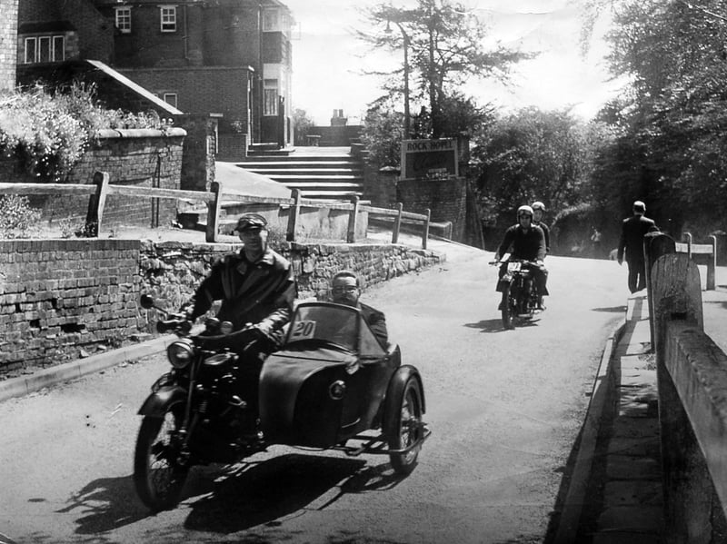 A 1928 AJS combination driven by R Jordan of Penn with John Priest, the owner, in the sidecar, motors past the Rock Hotel at Tettenhall, Wolverhampton. The print has a date stamp for May 18, 1964, but we haven't been able to identify this event, although as the magnificent machines have numbers on clearly it is some sort of rally or race.