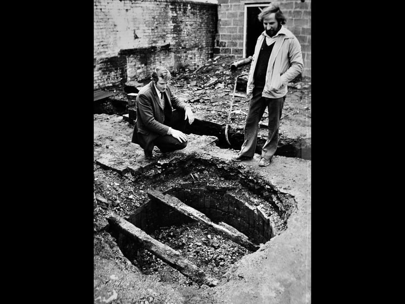 Keith Worrall and Alan Bennett examine an old well discovered during renovation work at the former stable block behind the Old Bell Inn in High Street in March 1978. The unexpected find left workmen wondering about the history hidden beneath the building. What do you think the well was once used for, and do you remember the Old Bell Inn before the changes?
