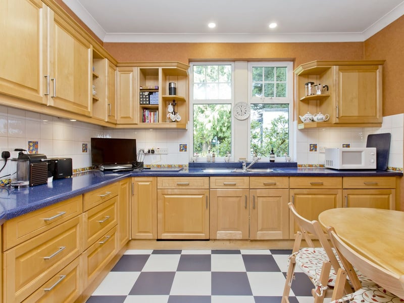 The generous breakfasting kitchen is fitted with an extensive range of timber cabinets, dark worktops, tiled splashbacks, a chequerboard floor, and a freestanding range-style cooker, with a window bringing in natural light and garden views. Its generous proportions allow ample space for informal dining. The practical layout is supported by a separate laundry room and side vestibule.