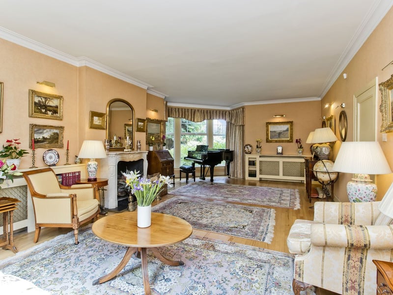 The drawing room forms an elegant setting for formal relaxation, with a broad bay window framing the garden and a working fireplace creating an inviting focal point.