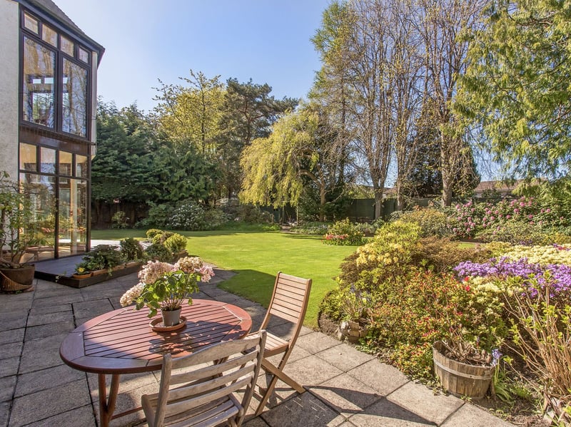 Sweeping lawns are framed by beautifully established beds filled with colourful shrubs, rhododendrons, and mature specimen trees, including a graceful weeping willow. Paved terraces and decking create several peaceful places for outdoor dining and relaxation.
