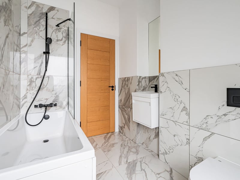 The main family bathroom, comprising an attractive three-piece white suite, fashionable wall and floor tiling, and an over-bath shower with splash screen.