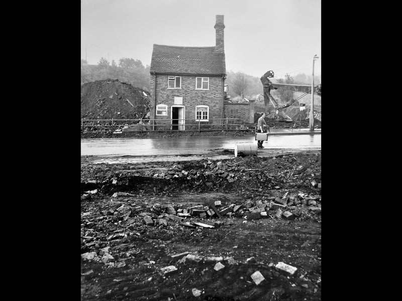 A solitary brick building housing a licensed betting shop stands isolated amidst earthmoving machinery and piles of rubble during the construction of the new Madeley bypass. Photographed on 20 September 1967, the striking scene captures heavy transformation in progress across the area. A worker carrying equipment walks past mud and debris as excavators carve out new road links, leaving old premises surrounded by cleared land as Telford's early infrastructure began taking shape. Do you remember watching the construction of the Madeley bypass in 1967, or do you recall this betting shop before the area was transformed?