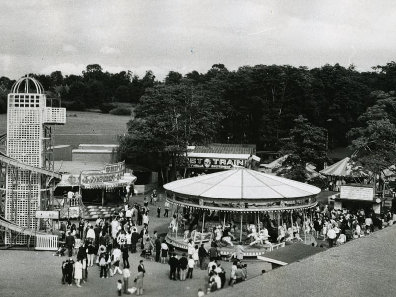 Families and thrill-seekers flock to the vibrant fairground rides at Drayton Manor Park near Fazeley in 1962. Founded just twelve years earlier in 1950 on the former estate of Sir Robert Peel, the park was rapidly expanding its attractions to become one of the region's top leisure destinations. This nostalgic aerial view captures classic vintage rides, including a towering helter-skelter, a spinning carousel, a ghost train, and traditional side stalls thronged with visitors enjoying a sunny day out. Do you have fond memories of visiting Drayton Manor Park back in the 1960s, or do you remember brave rides down that giant helter-skelter?
