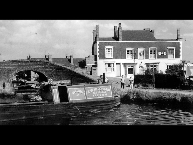 A narrowboat named Victory, operated by Tipton coal merchant C W Mitchard, glides past the iconic Beehive public house at Tipton Green Canal Junction in 1962. The Mitchells & Butlers pub stood alongside the Tipton Green Locks Branch, a historic waterway originally opened in 1805 to serve the region's bustling heavy industries. By the time this photo was taken, commercial traffic was rapidly fading, with the branch having been officially abandoned in 1960. The beloved local pub eventually closed its doors in 1978 before the entire site was redeveloped, leaving this quiet snapshot as a rare reminder of the area's industrial past. Do you remember enjoying a pint at The Beehive, or seeing the old coal boats working these waterways back in the day?