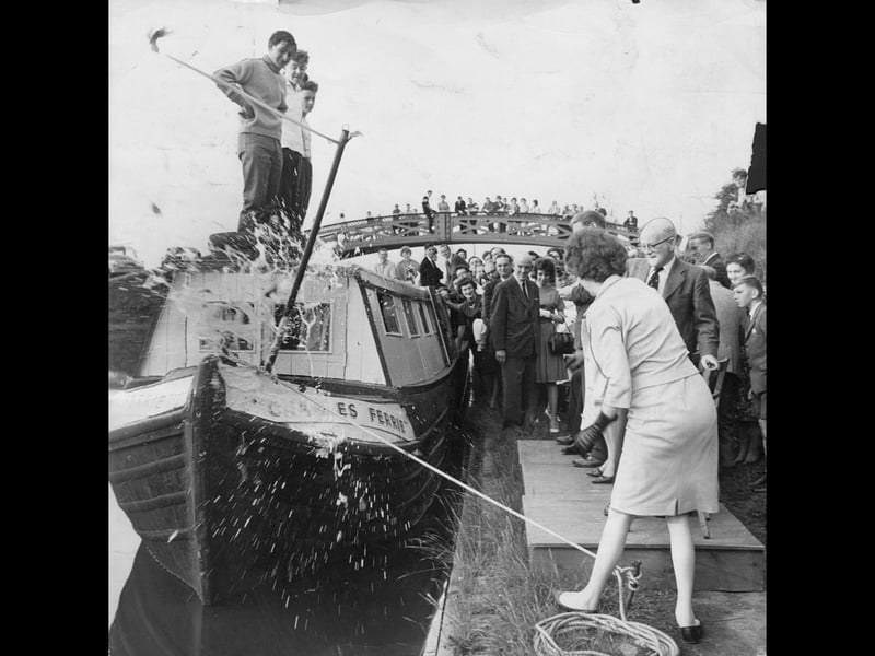 Champagne sprays dramatically across the bow as a newly launched boat is officially christened at Brownhills in 1962. It took four energetic swings before the stubborn bottle of 1953 vintage champagne finally shattered against the wooden hull, sending foam flying over the boat and delighting the crowd gathered along the canal bank and towpath bridge. Local dignitaries and eager young onlookers cheered on the ceremonial launch, capturing a wonderfully cheerful moment of Black Country community life along the canal. Were you in the crowd watching this lively canal boat launch at Brownhills in 1962?
