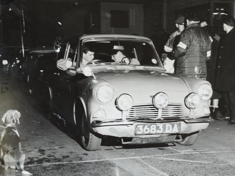 Bilbrook driver Richard Hill sits behind the wheel of his auxiliary-lamp fitted saloon car as he and his navigator confer ahead of a rally start in 1962. Surrounded by marshals, spectators, and even a curious dog sitting by the roadside, the crew prepares to tackle the dark country lanes against the clock. Local motorsport events were immensely popular across the region during the 1960s, drawing passionate driving enthusiasts and skilled navigators from villages across the Black Country and South Staffordshire. Do you remember attending nocturnal road rallies or competing in local motorsport events around the region in the 1960s?