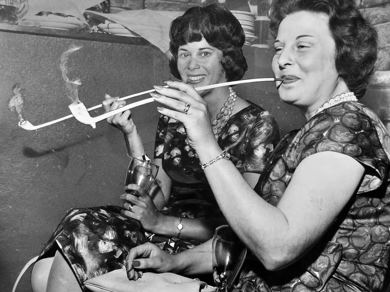 Mrs Patsy Smith (left) and a fellow contestant puff away on long-stemmed clay churchwarden pipes during a quirky contest held at a Wall Heath club in June 1962. Charged with just 3.3 grams of tobacco, the goal was to keep the pipe lit as long as possible, with Mrs Smith managing an impressive 34 minutes of continuous smoking. The novel event saw local women join in the friendly competition, providing plenty of amusement and lighthearted entertainment for the evening's club goers near Kingswinford. Do you remember attending any unusual novelty contests or social club events around Wall Heath in the 1960s?