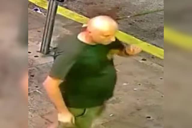 Bald man, green t-shirt with logo lefthand side of chest, khaki shorts and sandals.