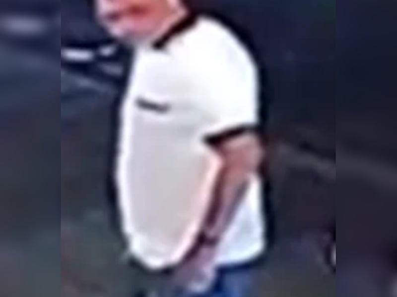 Bald man, white t-shirt with black collar and cuffs, jeans.