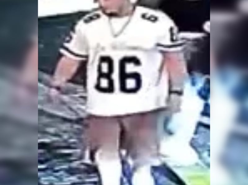 Man with dark hair, goatee, white t-shirt with “86” in black writing, brown shorts.