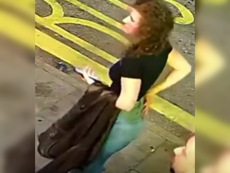 Woman with curly hair, black t-shirt and jeans, carrying a jacket.